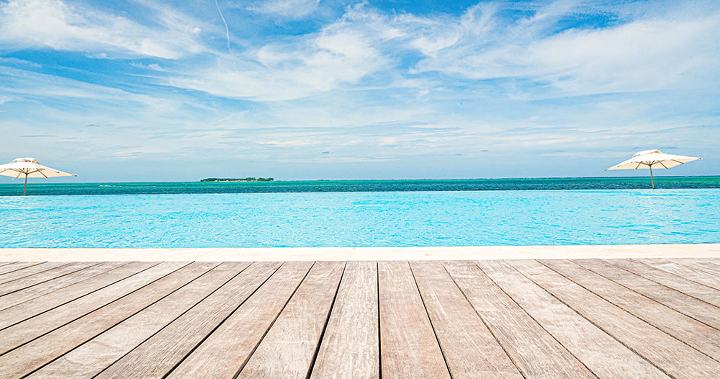 Wooden deck overlooking a clear blue ocean with two umbrellas and a distant island.