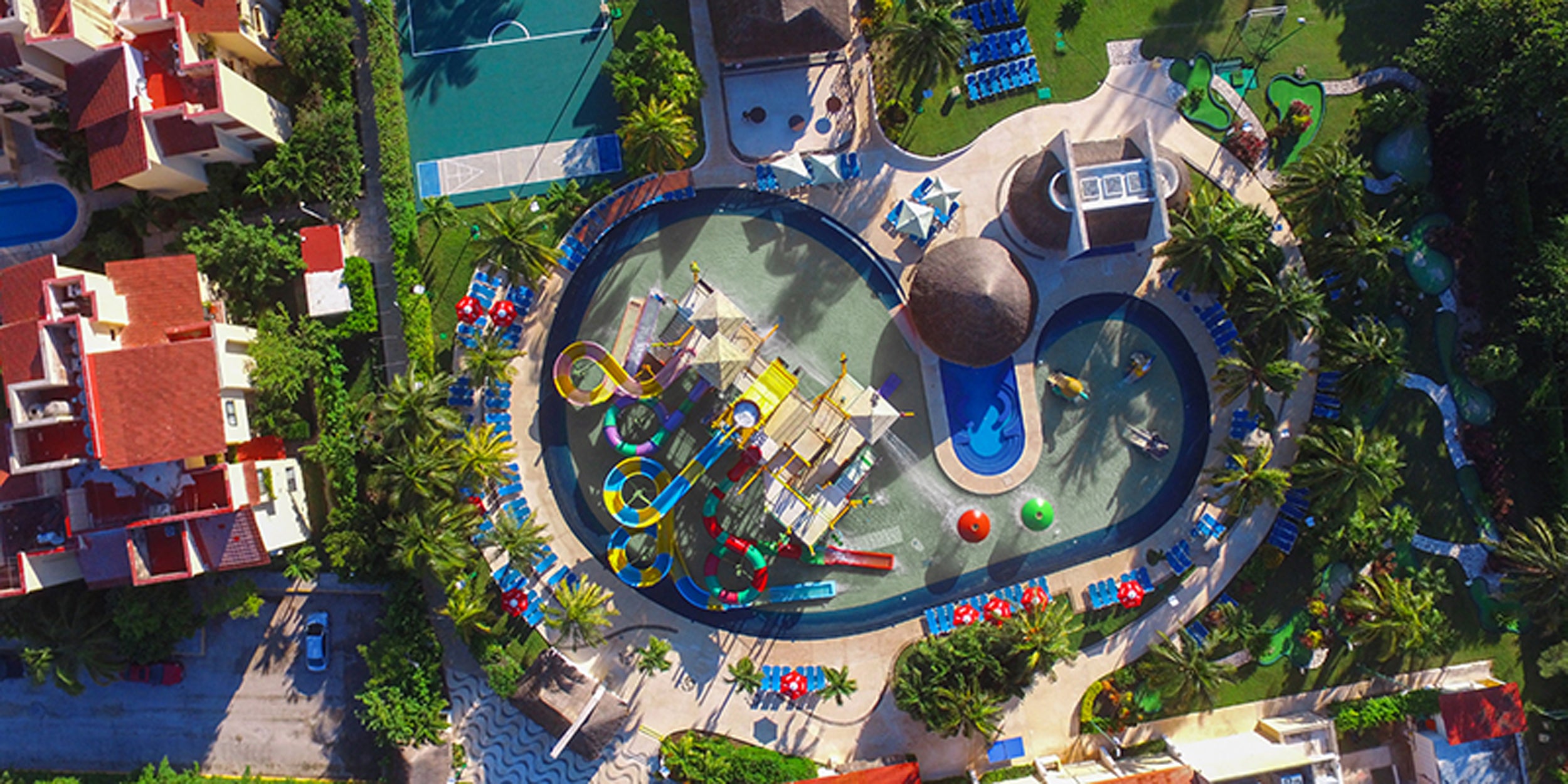 Aerial view of a resort with a large pool area, slides, and surrounding buildings.