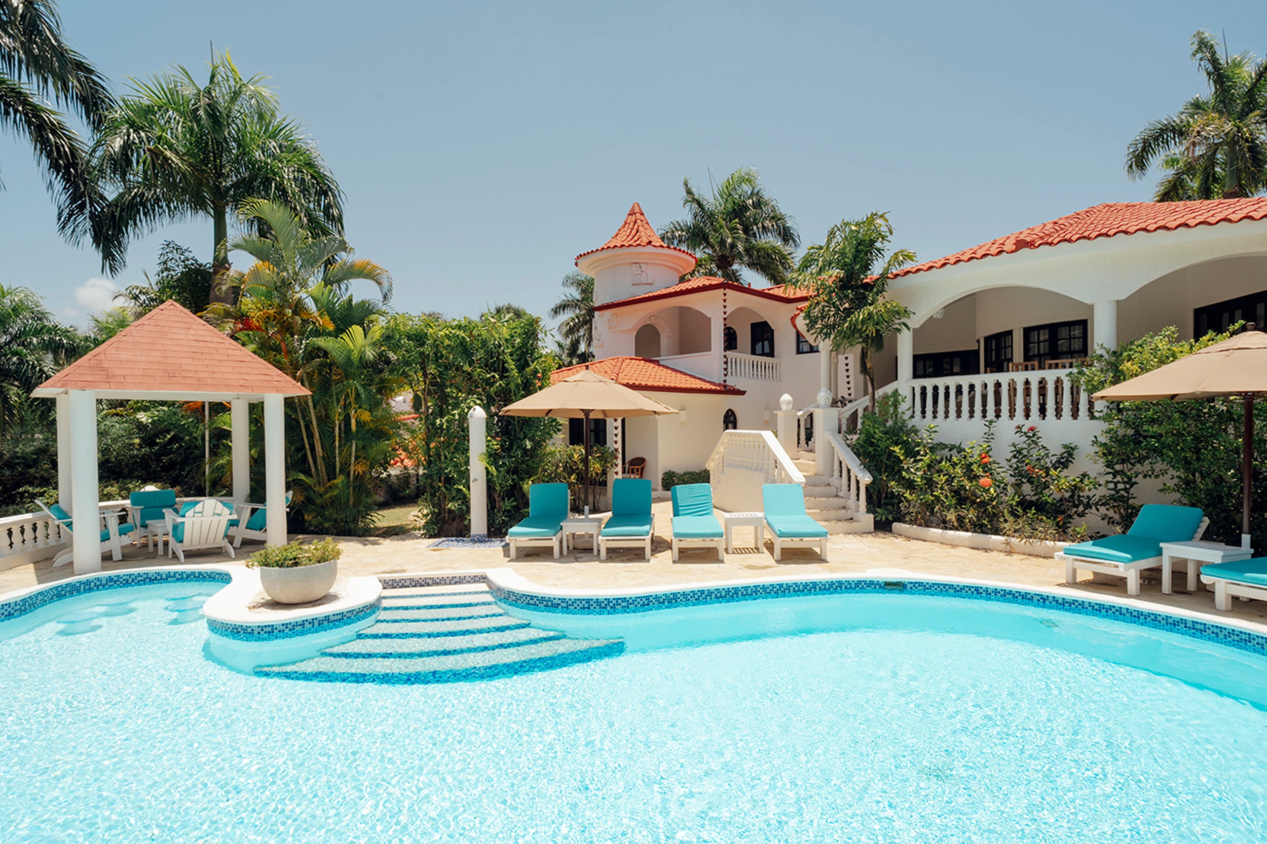 Pool area with lounge chairs, gazebo, and house in the background.