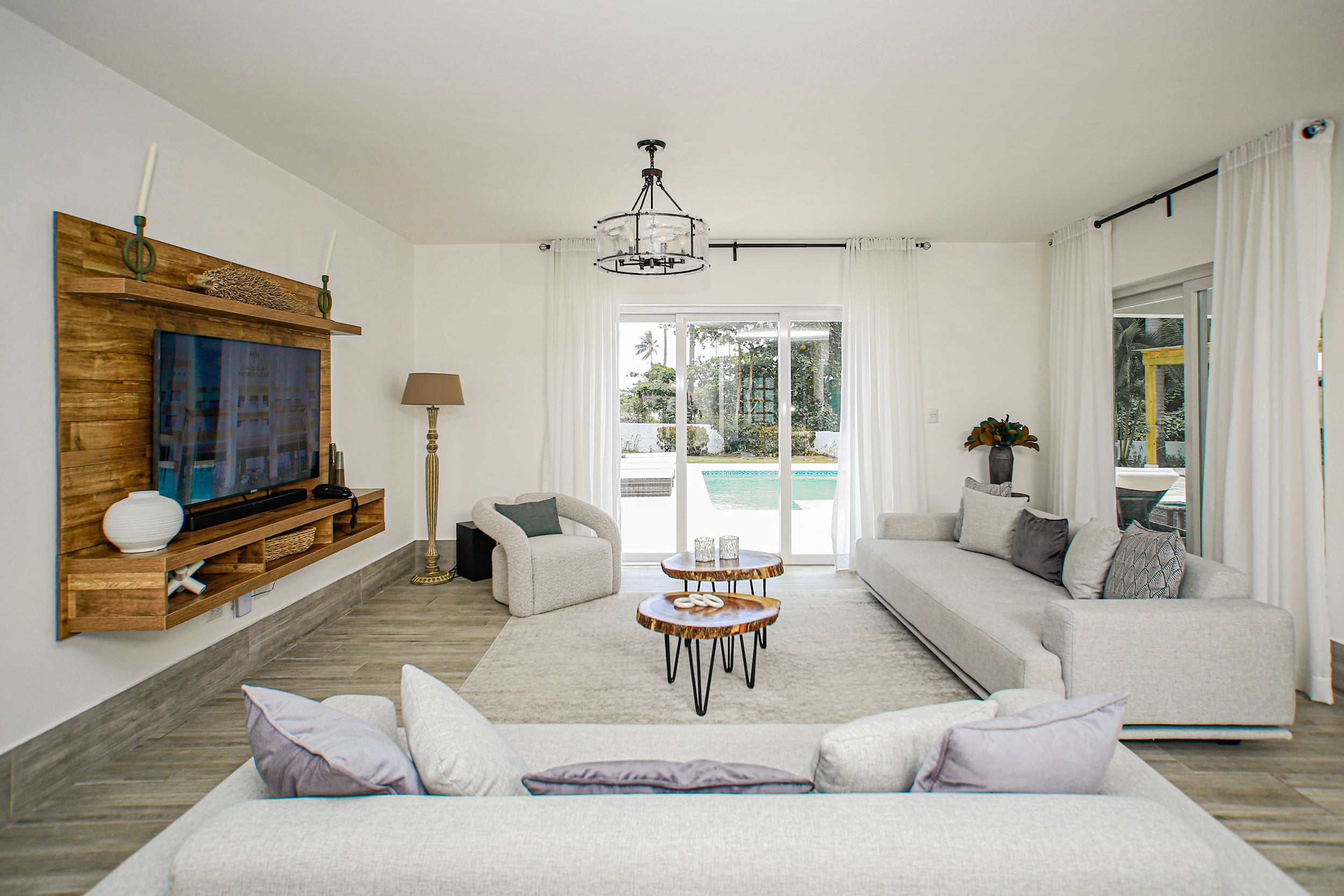 Modern living room with white furniture, wooden TV stand, and outdoor view.