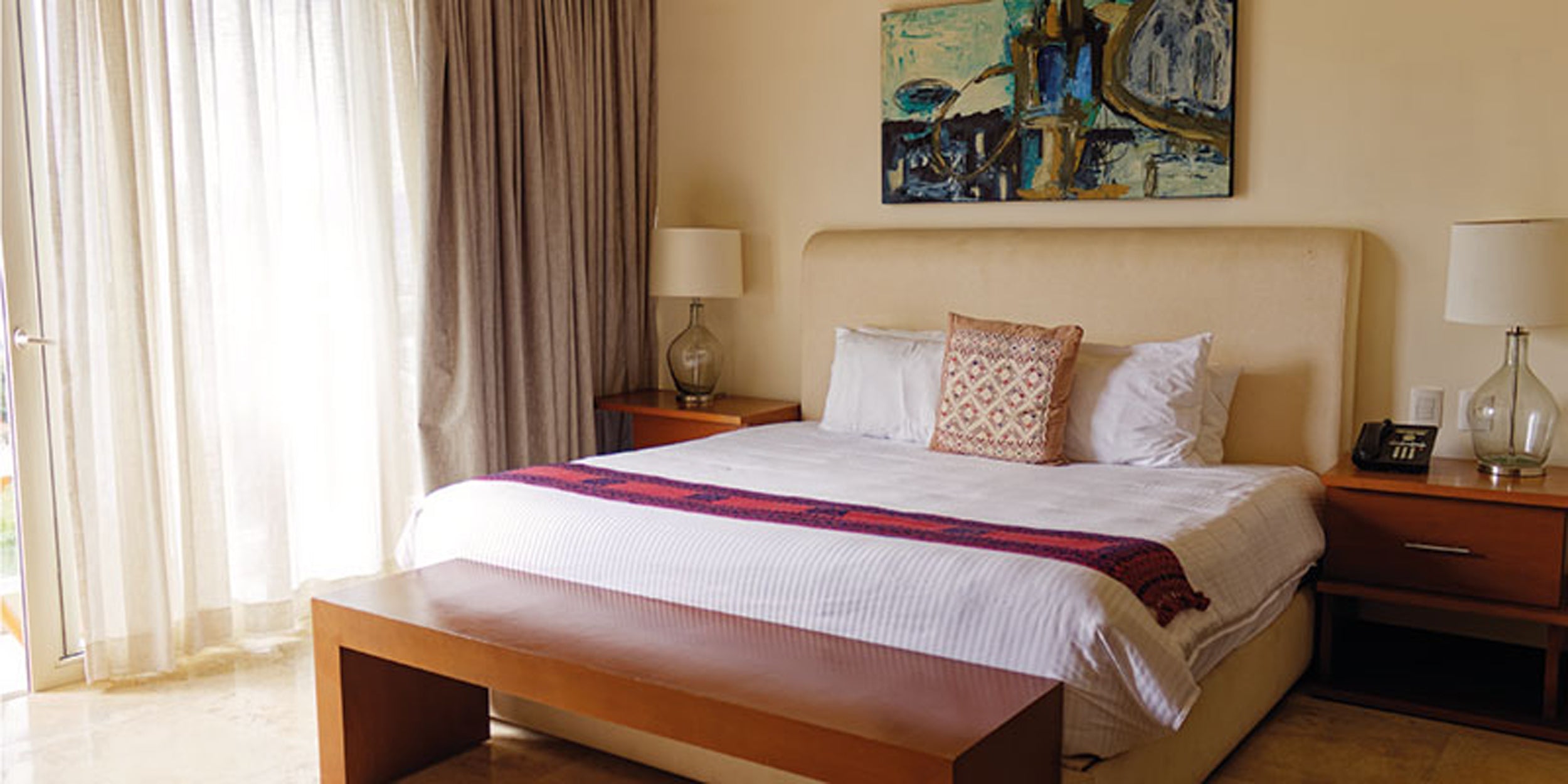 Neatly made bed in a bedroom with decorative pillows and a painting on the wall.