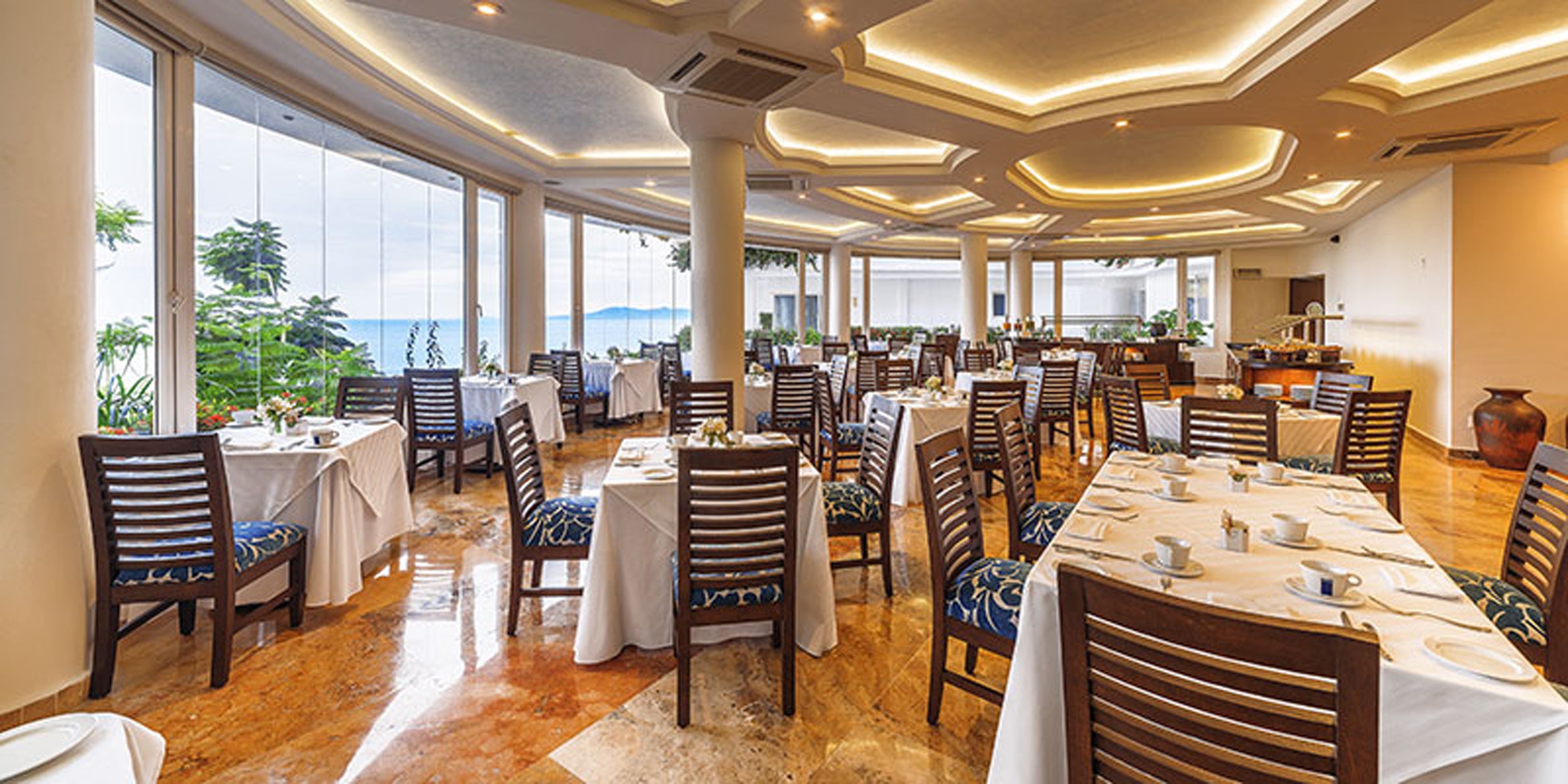 Restaurant interior with tables, chairs, and large windows overlooking a scenic view.