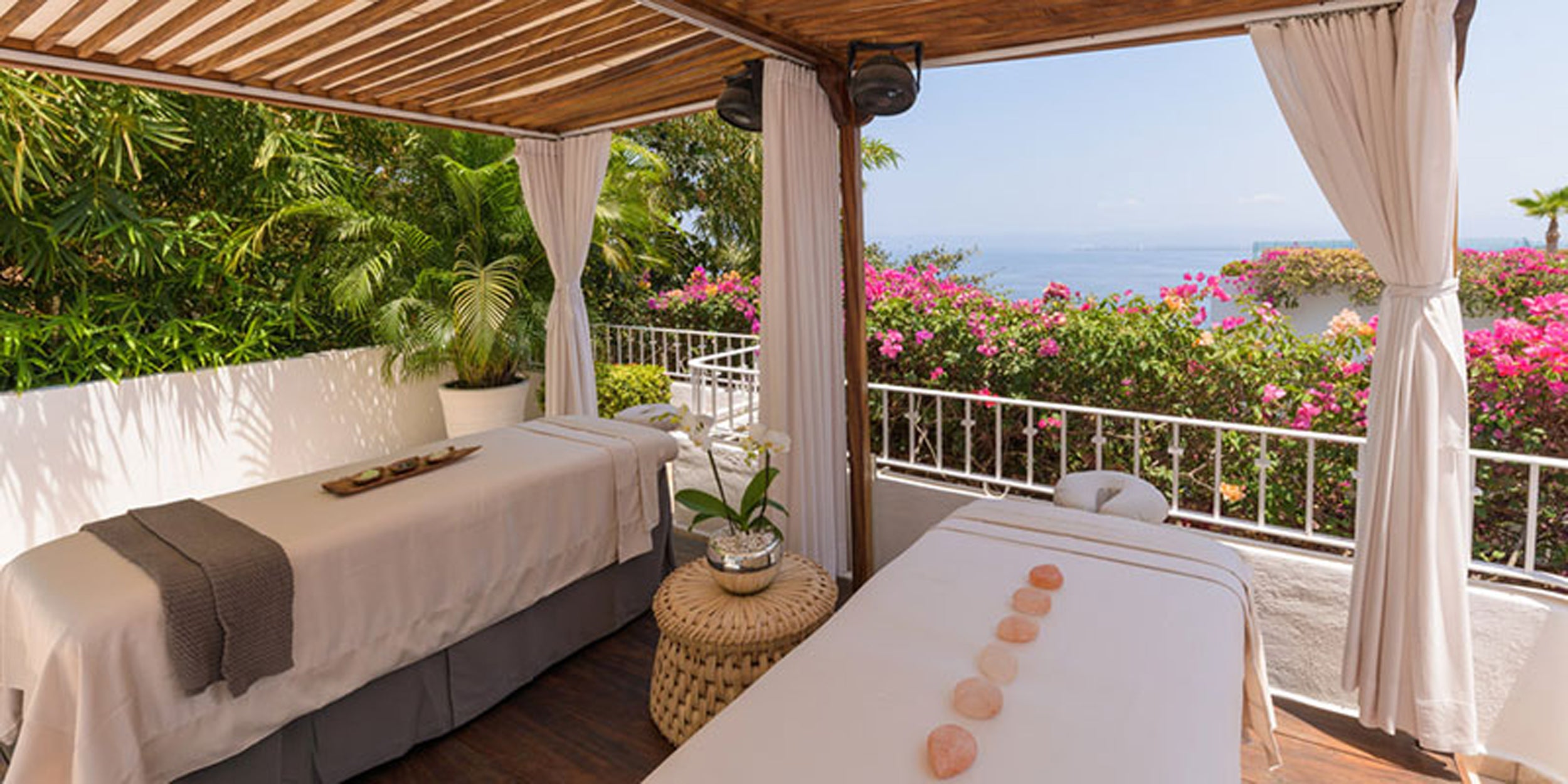 Spa treatment room with ocean view, white beds, and floral decorations.