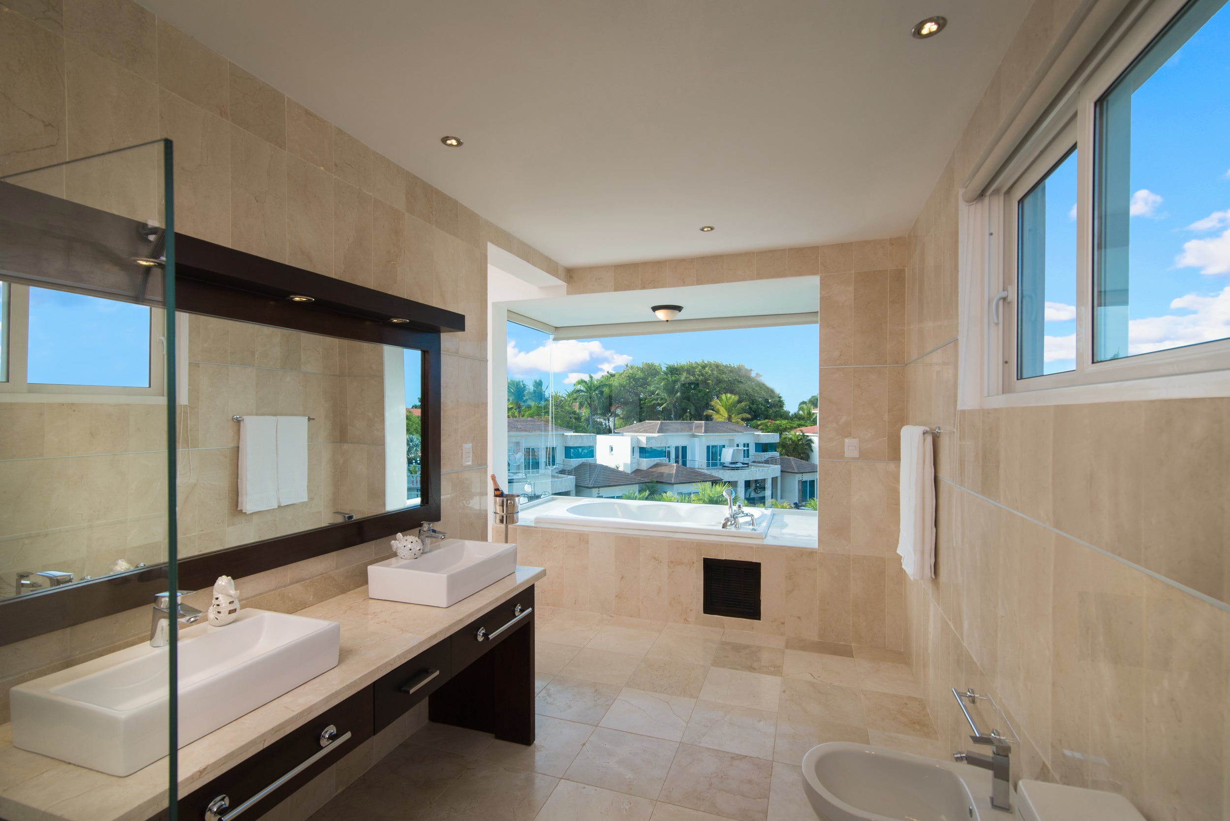 Modern bathroom with large windows, beige tiles, and a view of trees.