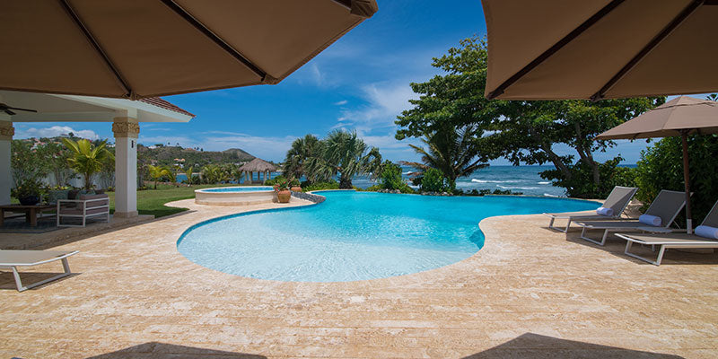 Pool area with lounge chairs, umbrellas, and a scenic view of trees and water.