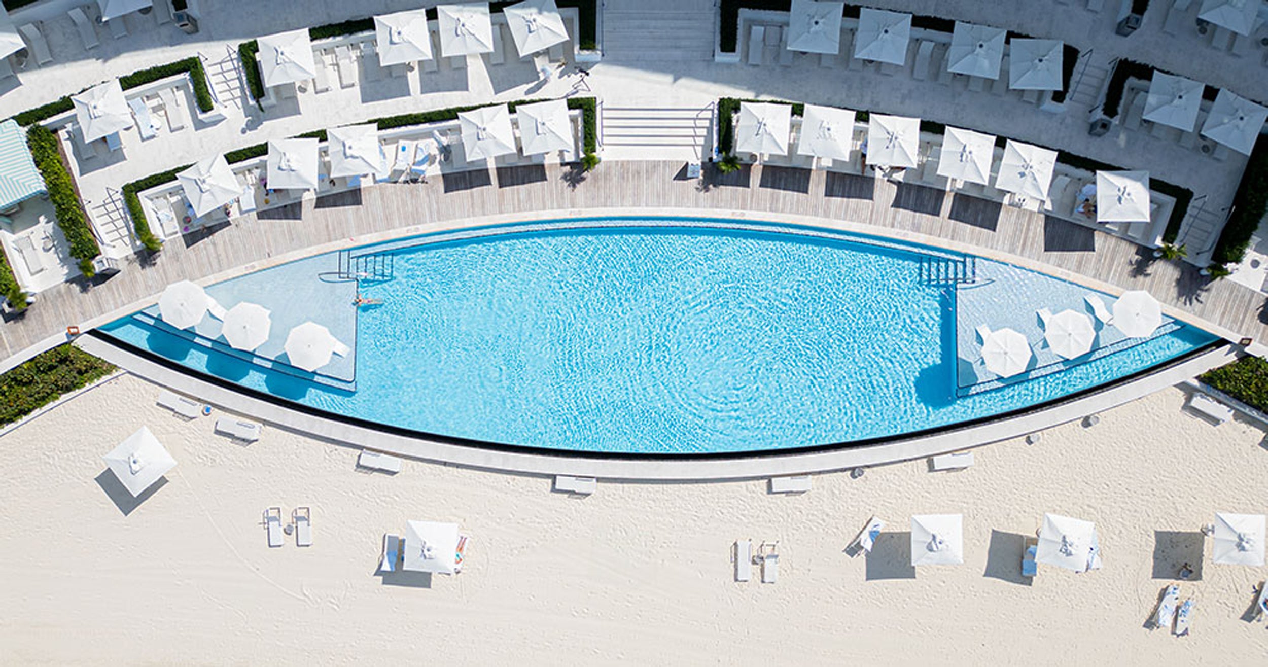 Aerial view of a large pool with lounge chairs and umbrellas around it.