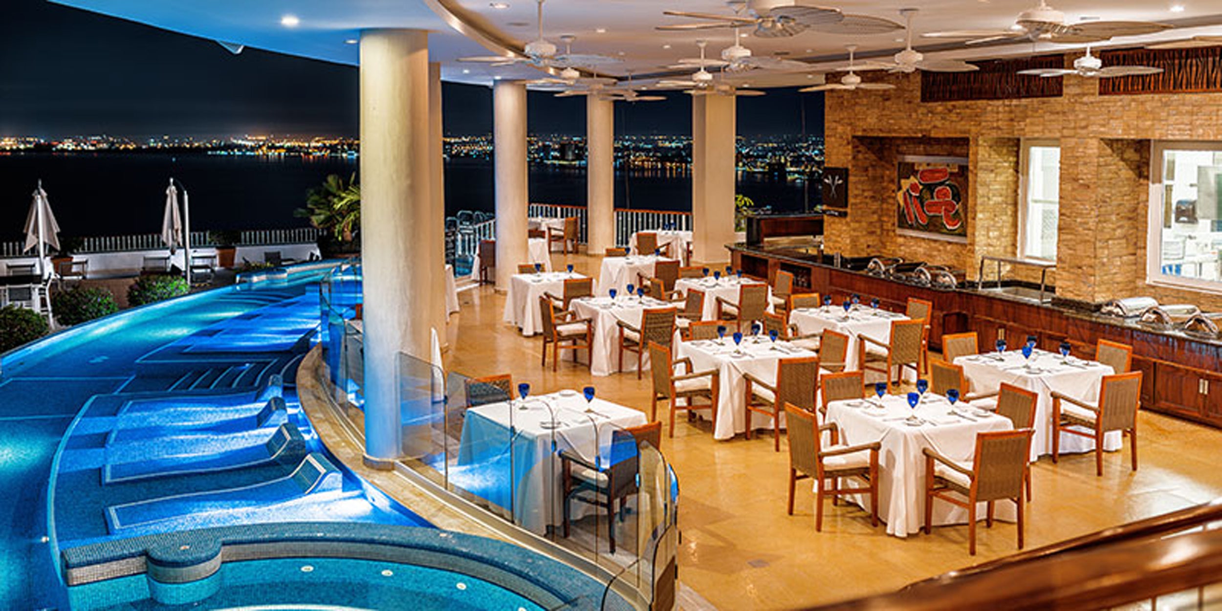 Luxury restaurant with poolside tables and a scenic view at night.