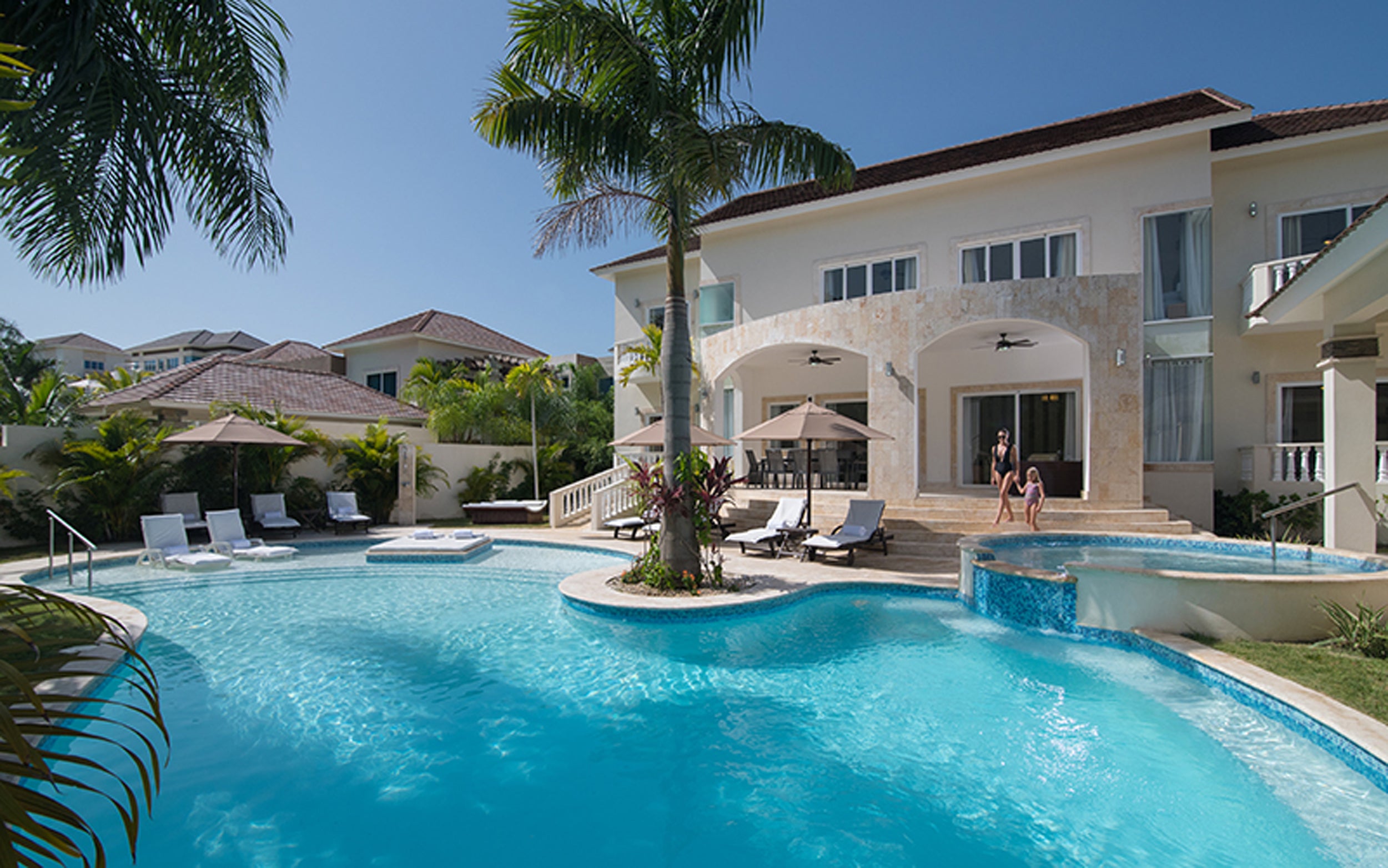 Royal Villa with a large pool and palm trees on a sunny day.