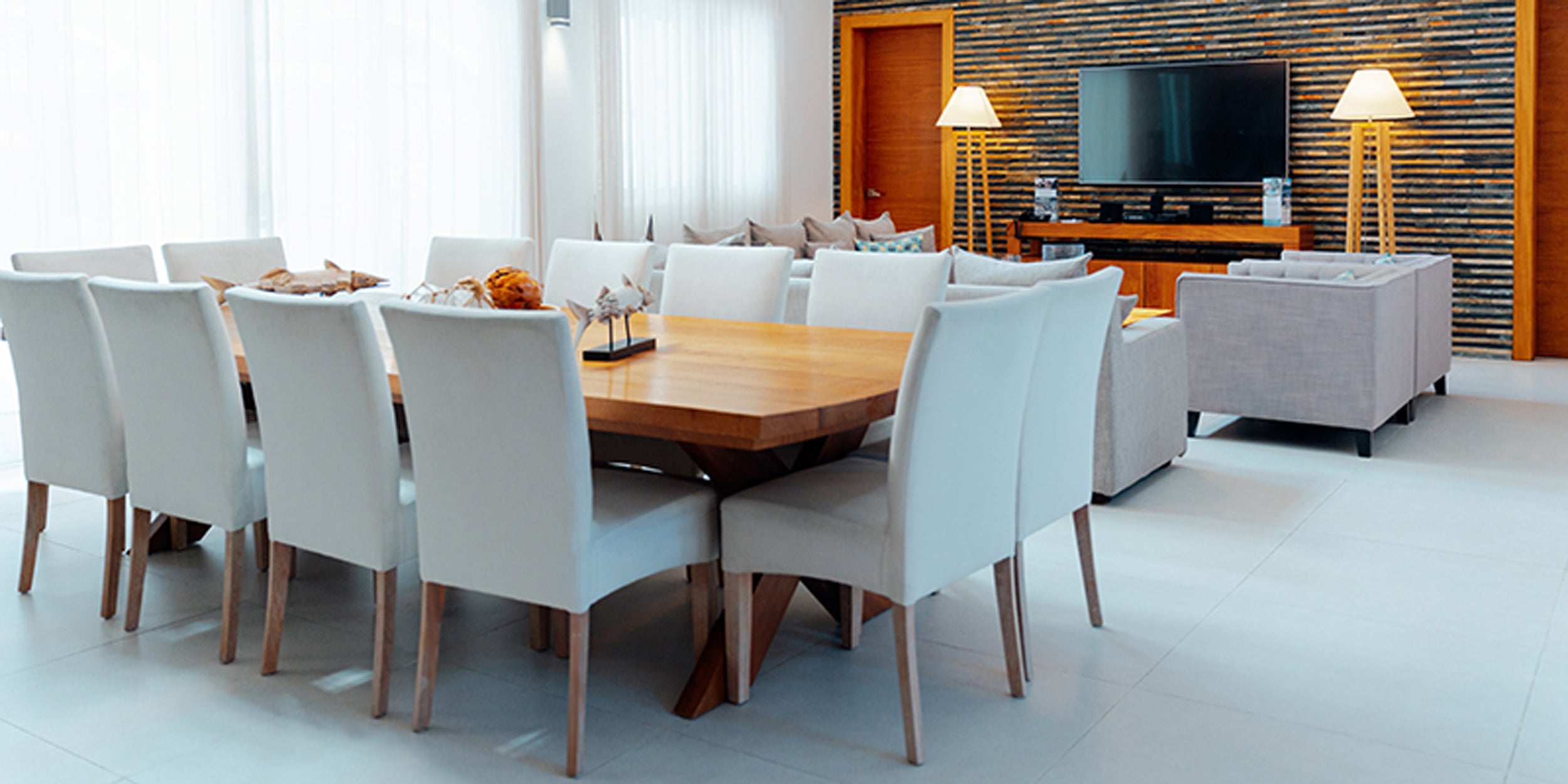 Modern dining room with a wooden table and white chairs, featuring a television and decorative items.