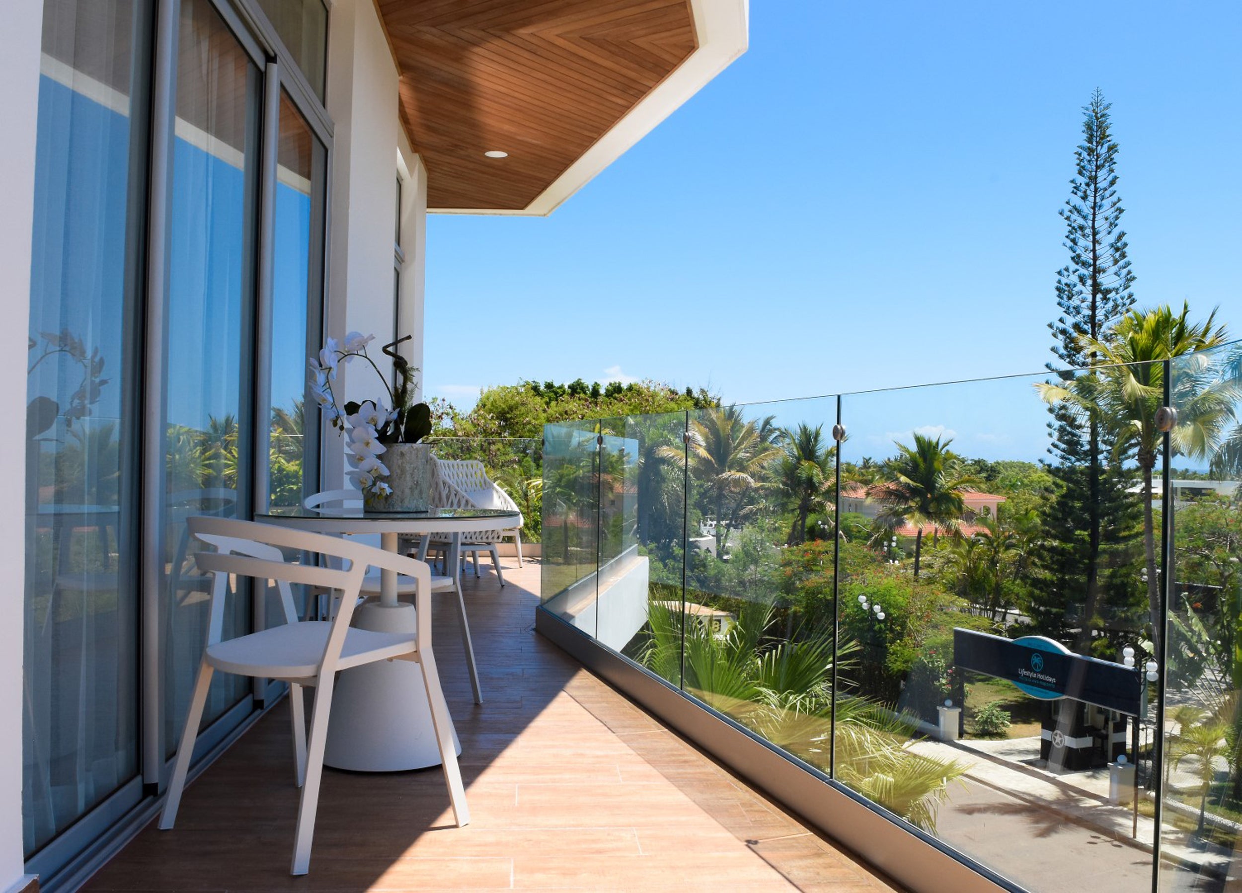 Balcony with glass railings, white chairs, and a view of greenery