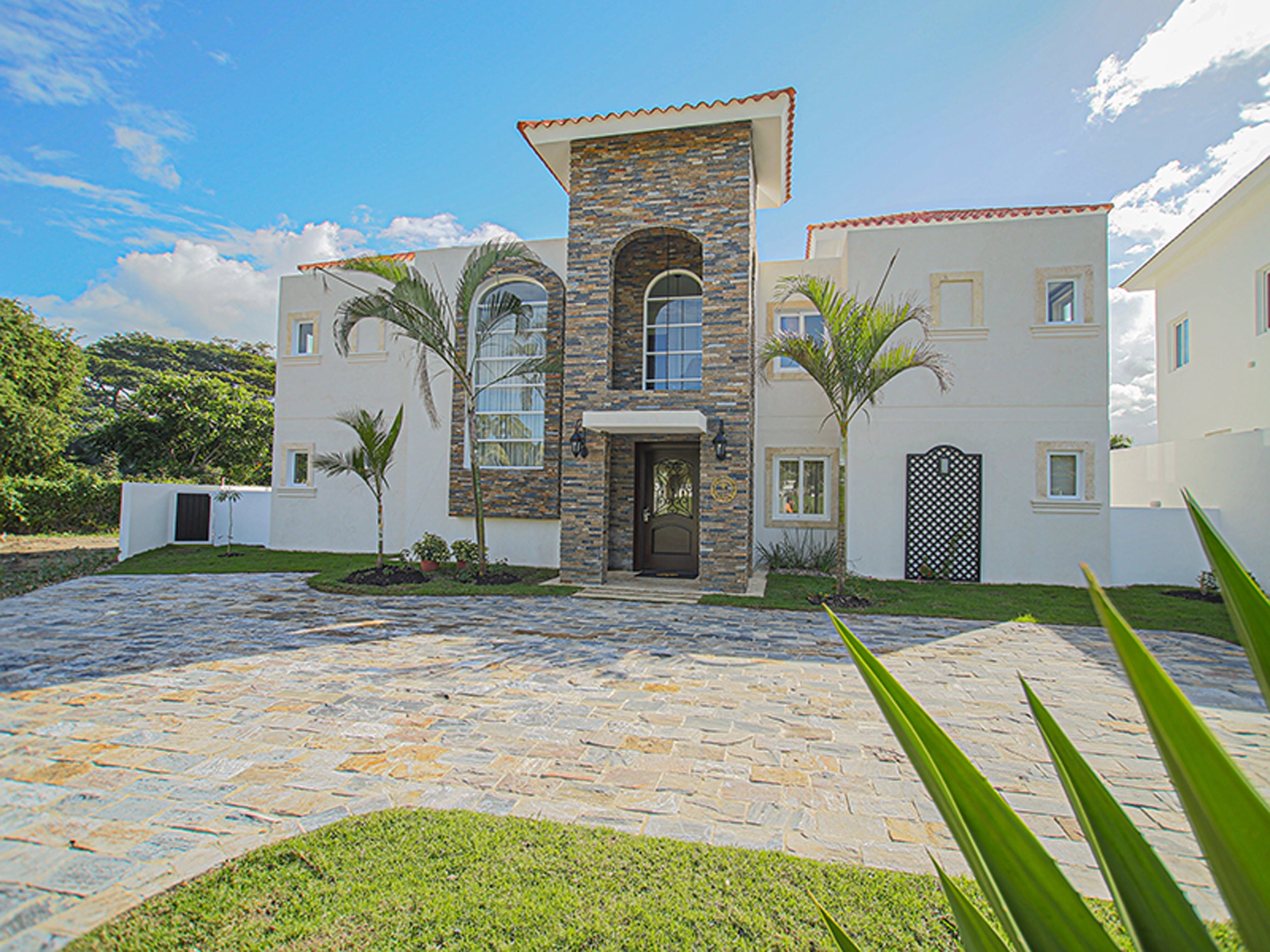 Two-story villa with stone facade and palm trees on a sunny day