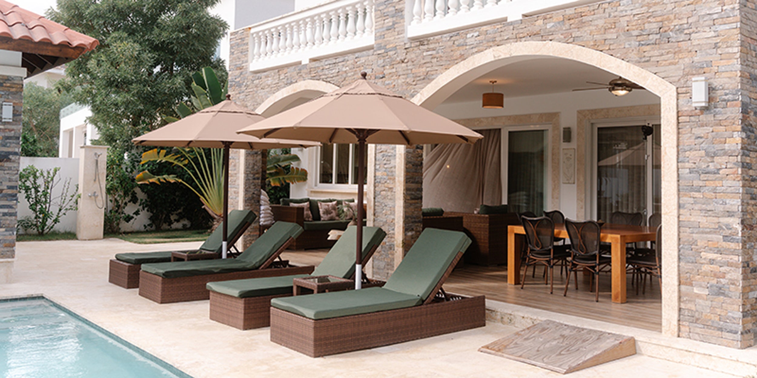 Outdoor patio area with lounge chairs, umbrellas, and a pool near a house.