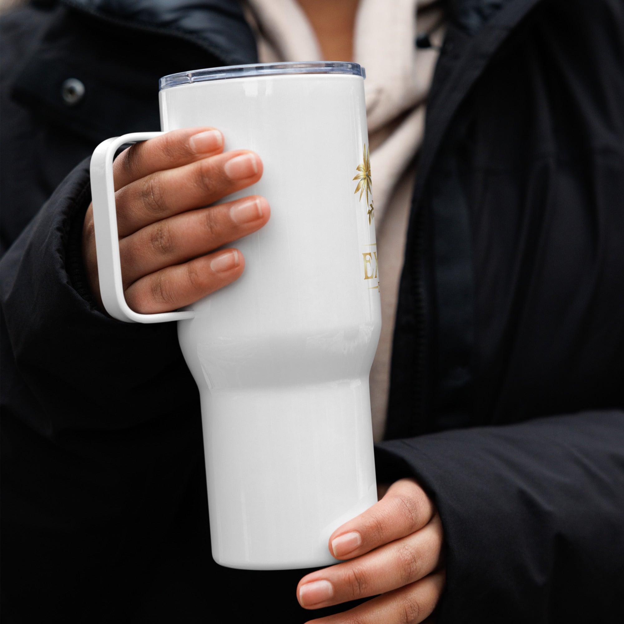 Person holding a white tumbler with a logo in a blurred outdoor setting